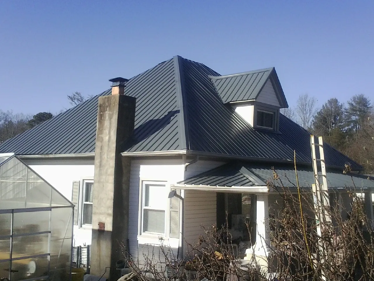 Dark blue standing seam metal roof on a white farmhouse with dormer — Slate & Tile Roof Repair by Roofing Brothers in Center Junction