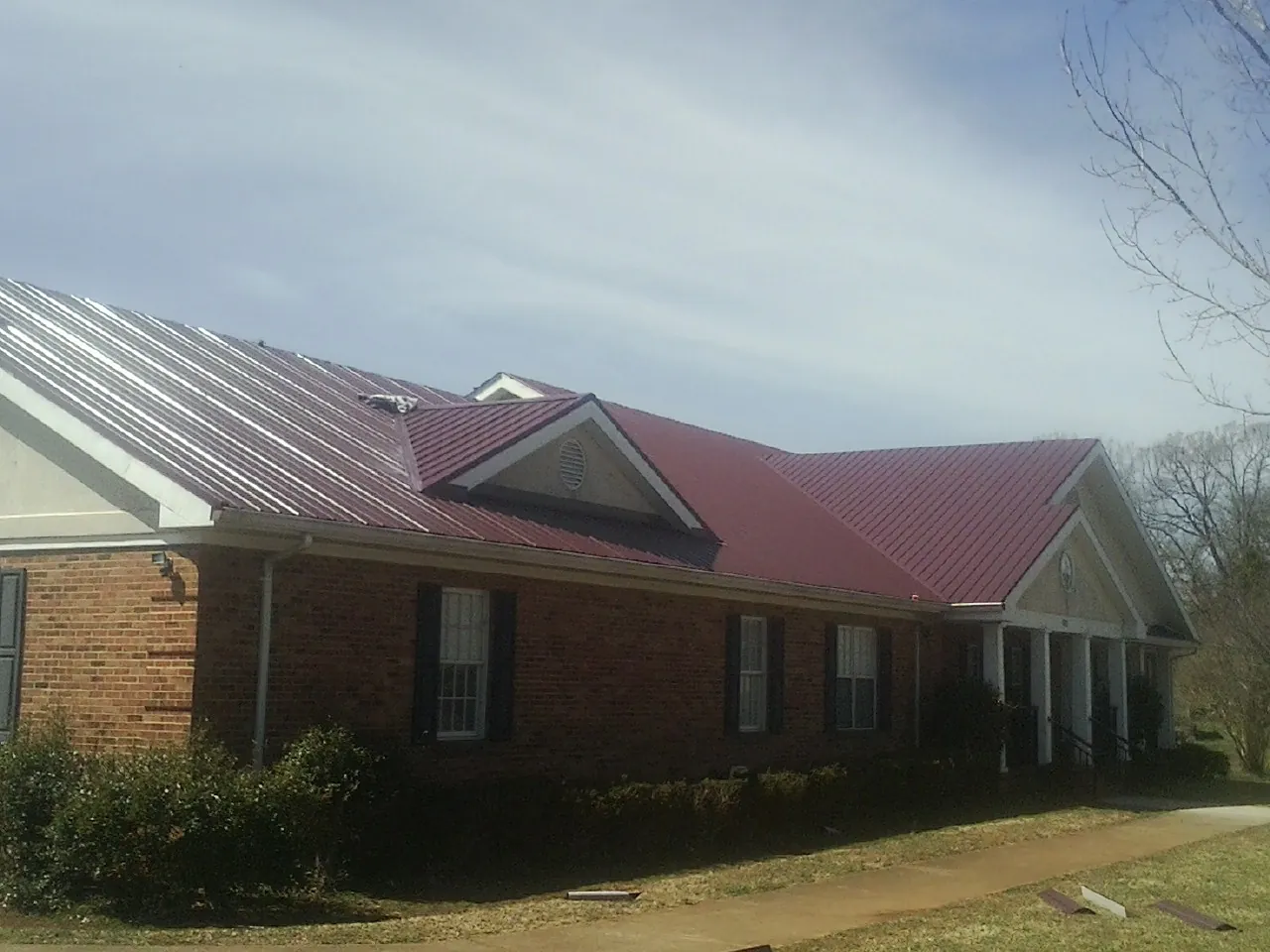 Red metal roof with gabled entries on a long brick building, from a Hail Damage Roof Repair job in Center Junction