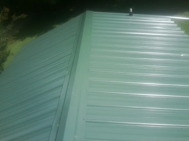 New green metal panels meeting at the ridge of a roof — Flat Roof Repair work by our crew in Center Junction