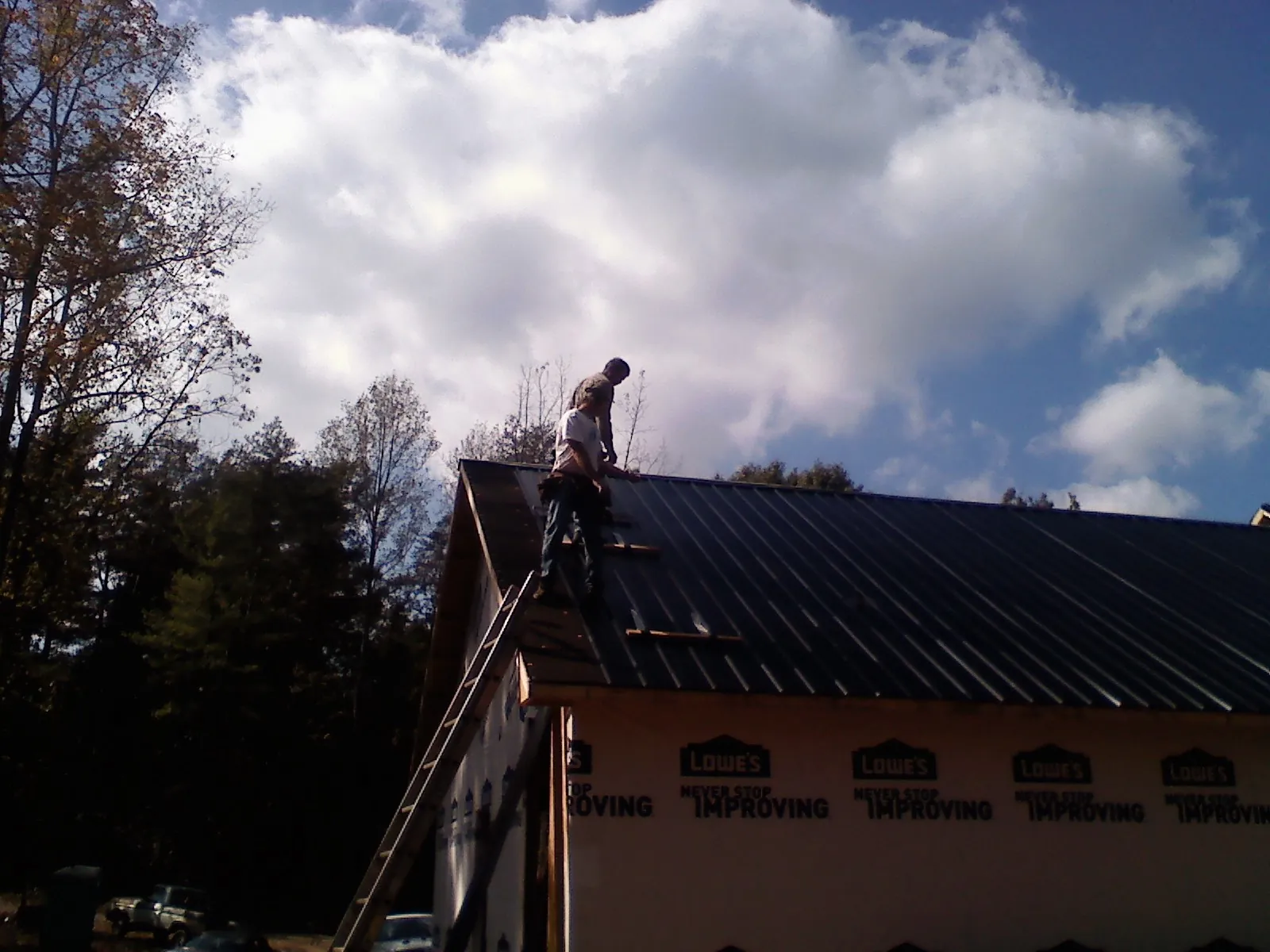 Roofer fastening dark metal panels high against a cloudy sky, from a Roof Inspection job in Center Junction