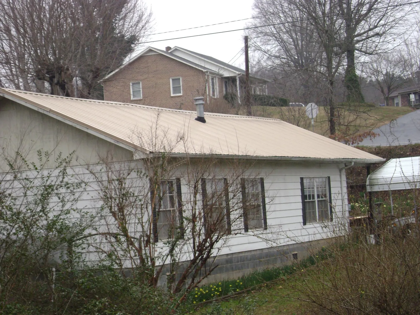 Tan metal roof on a white sided house set into a hillside — Commercial Roofing by Roofing Brothers in Center Junction